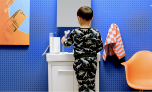 boy standing in front of sink in bathroom brushing his teeth